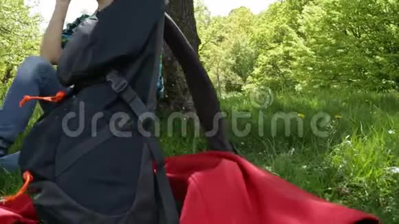 一个背着背包坐在树下喝水的女人视频的预览图