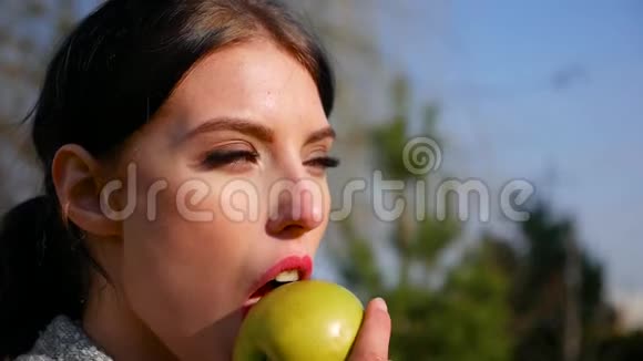 动作缓慢特写迷人的年轻黑发女人美丽的眼睛和红唇吃绿苹果视频的预览图