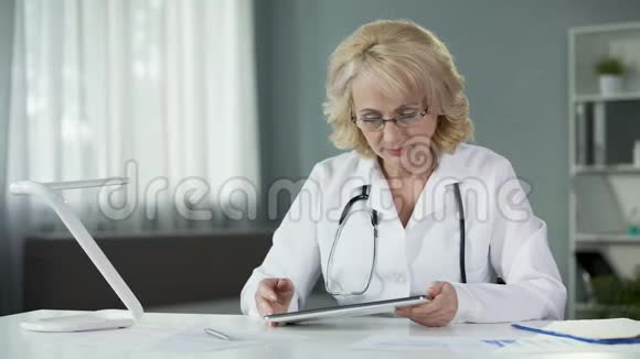 女性全科医生在平板电脑上阅读病人的在线病历视频的预览图