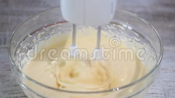 女人的手在厨房的碗里用搅拌器打面团视频的预览图