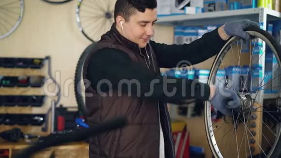 年轻的修理工正在清洗自行车车轮内外的脏布并用耳机听音乐视频的预览图