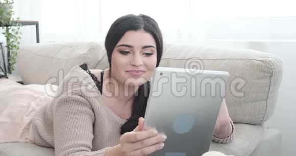 在家里沙发上使用数码平板电脑的轻松女士视频的预览图