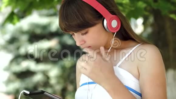 戴着耳机听音乐的小女孩在平板电脑上走来走去特写视频的预览图