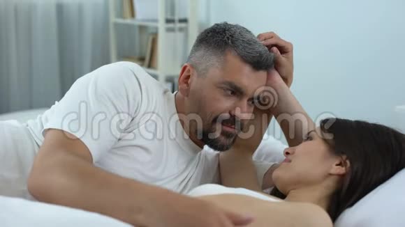 有爱心的丈夫欣赏他美丽的妻子新婚夫妇在床上蜜月时间视频的预览图