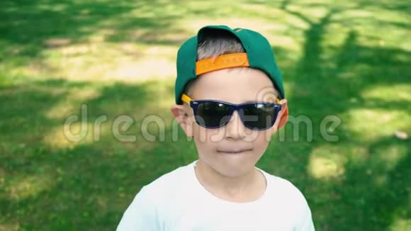 一个5岁的小男孩戴着太阳镜站在夏天的公园里开始嘲笑一个人他的真实情感视频的预览图