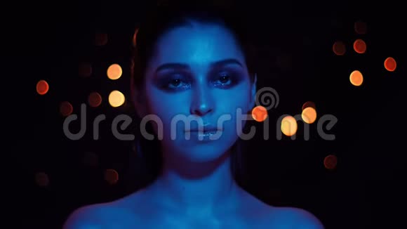 年轻漂亮的白种人女性的特写镜头配上蓝色霓虹灯和bokeh背景的漂亮妆容视频的预览图