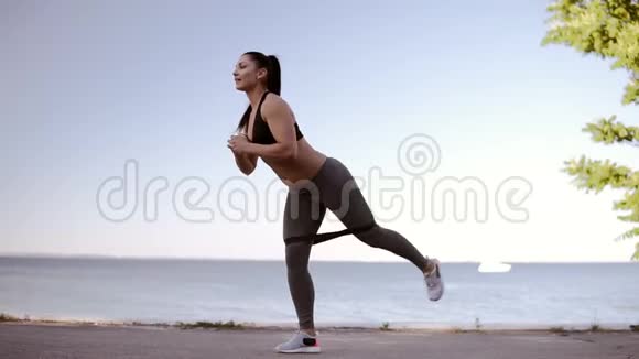 美丽的健身女孩在海滨做运动一个职业运动女性伸展双腿的长度视频的预览图