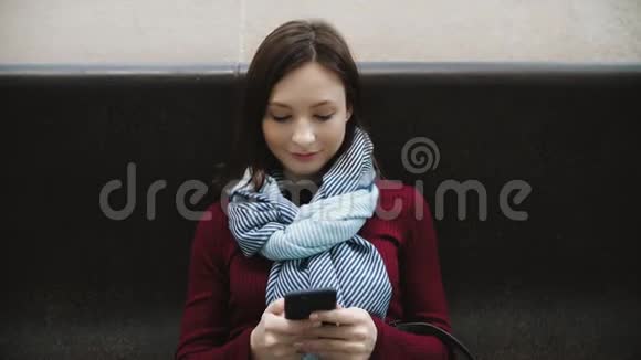 坐在地铁站大理石长凳上的兴奋的女人在智能手机上发短信视频的预览图