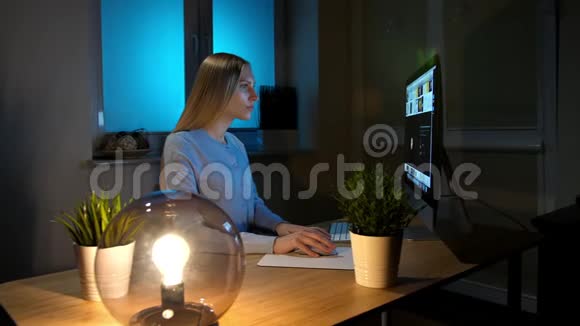 女人晚上专心看电脑穿着温暖的家居服坐在木制椅子上的美丽金发女性放松视频的预览图