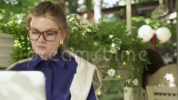 在夏天的咖啡馆里一位戴着笔记本电脑的眼镜的年轻女子被吸了一口气视频的预览图
