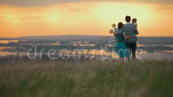 一家三口人在大自然中休息爸爸妈妈和儿子一起去拥抱橙色的日落视频的预览图