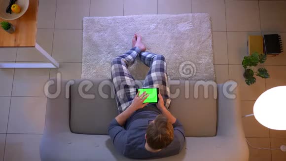 在舒适的家中年轻的穿着随意的男性使用平板电脑坐在沙发上的特写镜头视频的预览图