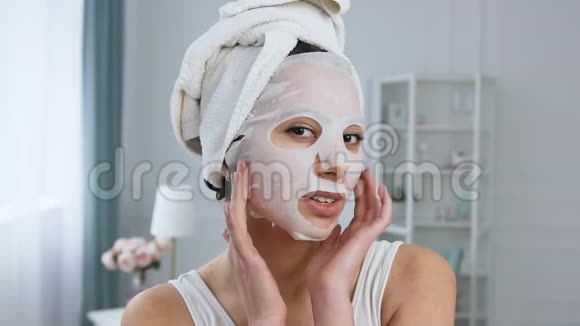 美丽的年轻女人的肖像在脸上固定恢复活力的化妆品白色组织面具视频的预览图
