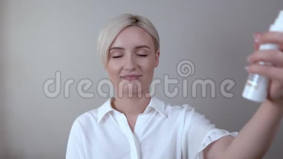 一个年轻的金发女人的特写用化妆固定喷雾在她的脸上视频的预览图