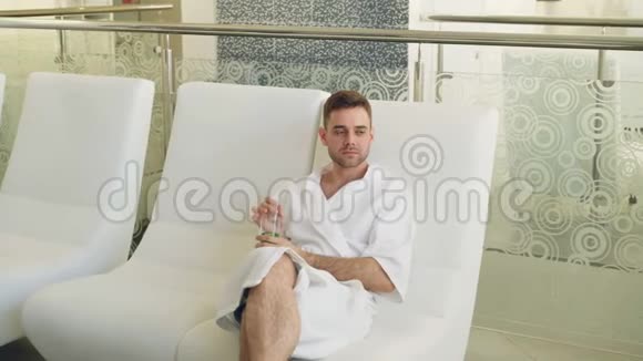 穿着浴袍的年轻人当他的女朋友来的时候正坐在日光浴的休息室里亲吻他和他说话视频的预览图