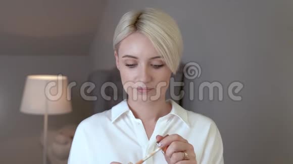年轻的短头发的金发女人在她的脸上涂上遮瑕膏视频的预览图