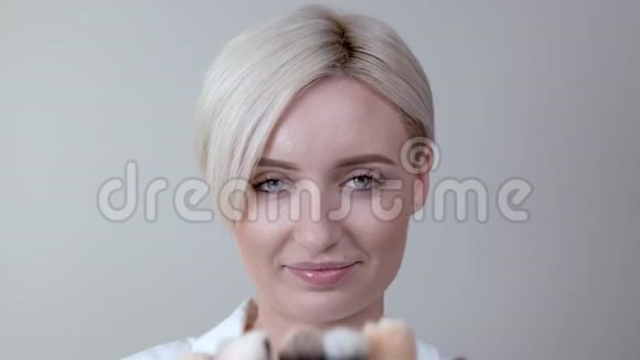 一位留着短发的金发女孩的特写镜头展示了她收集的日常化妆用品必备的画笔视频的预览图