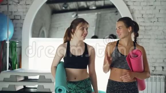 年轻漂亮的女运动员们穿着时髦的运动服在练习结束后手里拿着瑜伽垫离开健身房时会说话视频的预览图
