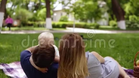 有爱心的年轻家庭和小儿子在户外野餐绿色公园野餐毯和装满水果的篮子视频的预览图