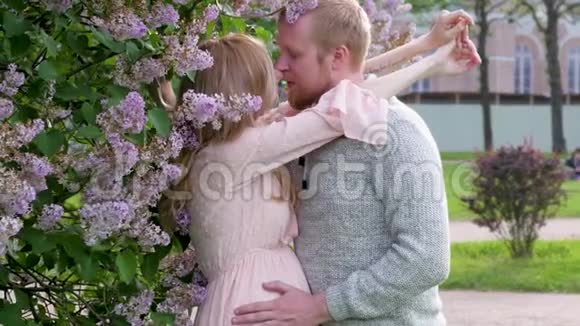 一个穿着粉红色裙子的孕妇正在公园的背景上拥抱她的丈夫等待孩子的年轻家庭视频的预览图