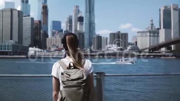 纽约著名的曼哈顿天际线上年轻快乐的旅游女孩背着背包双臂张开充满欢乐视频的预览图