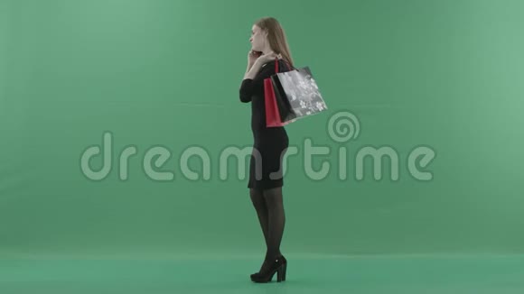 穿着小黑裙子的漂亮女人拿着购物袋在手机上说话她站着视频的预览图