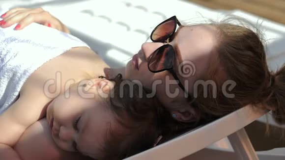 年轻妈妈和小女孩睡在露天游泳池的休息室里视频的预览图
