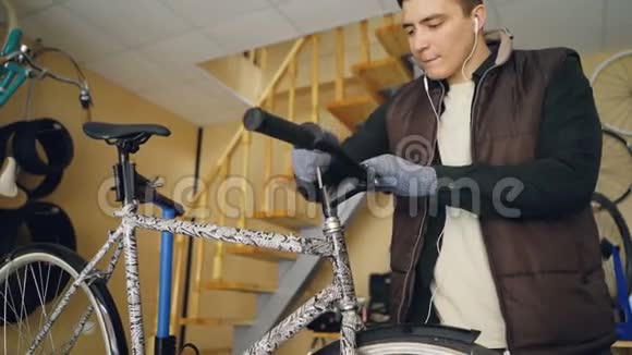 专注的男机修工正在用耳机听音乐同时固定自行车车把将其从车架上松开视频的预览图