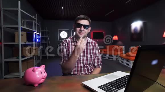 有胡子的年轻人带着太阳镜对着镜头说话有猪和笔记本电脑视频的预览图