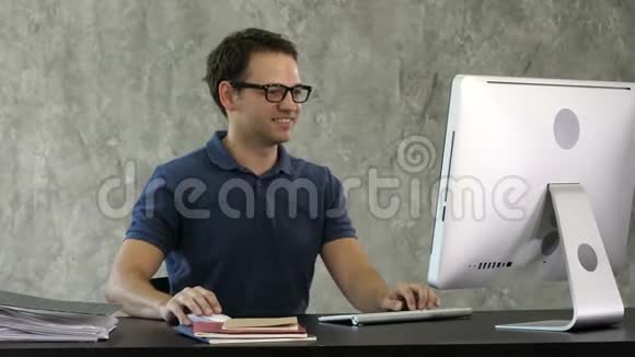 微笑的年轻人坐在办公室的办公桌前在电脑上工作视频的预览图