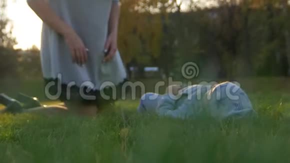 年轻的母亲带着她的小宝宝在日落时在秋天的公园里玩耍婴儿躺在草地上幸福家庭视频的预览图