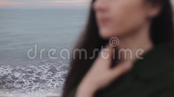 一幅模糊的近景一个穿着深绿色外套的漂亮女孩在海边摸着她的脖子焦点从视频的预览图