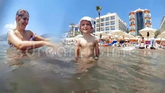 慢动作视频欢快的笑着蹒跚学步的男孩和妈妈玩耍在海里泼水视频的预览图