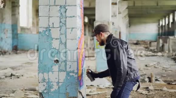 一个留着大胡子的帅哥拿着喷漆在宽敞的废弃房子里的柱子上涂鸦创造性的视频的预览图