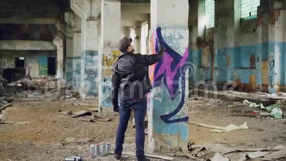 在宽敞的废弃建筑中穿着休闲服的涂鸦画家正在用喷漆在柱子上画画摘要视频的预览图