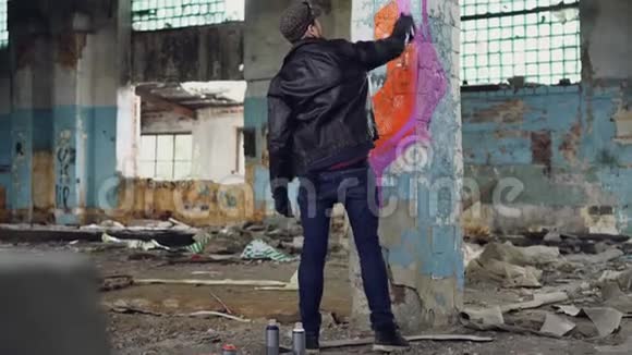 年轻人涂鸦艺术家正在用喷雾漆在旧的肮脏建筑的柱子上作画他穿的是一身视频的预览图