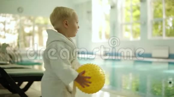 可爱的小男孩在休闲中心向游泳池投掷一个黄色的球室内游泳池穿小白衣服的男孩视频的预览图