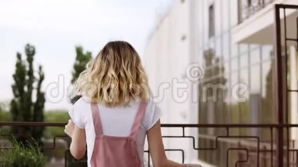 年轻漂亮的金发女孩正从阳台上洒出纸屑喊她的女朋友所有人视频的预览图