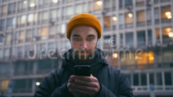 晚上帅哥在城市大街的智能手机上浏览互联网视频的预览图