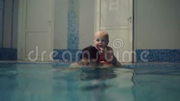 年轻人潜入水中在封闭的游泳池里划船小男孩在他父亲的背上微笑母亲视频的预览图