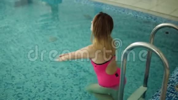 一位穿着粉红色泳衣和长发的漂亮年轻女子正在室内的小游泳池游泳很放松慢慢视频的预览图