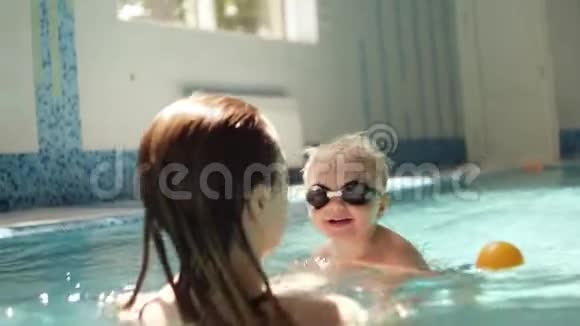年轻女子抱着儿子教游泳支撑在水面之上室内游泳池游泳的小男孩视频的预览图