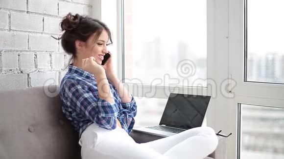 漂亮的女人坐在沙发上在客厅的家里用笔记本电脑打电话视频的预览图