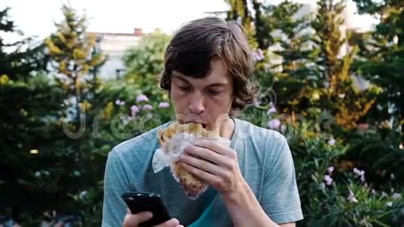 男人使用智能手机吃卡查普里面包街上有肉或豆子动作缓慢视频的预览图