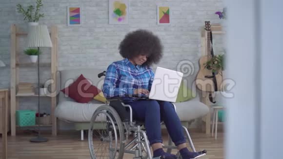 残疾的非裔美国妇女头发是非洲的坐在轮椅上使用笔记本电脑视频的预览图