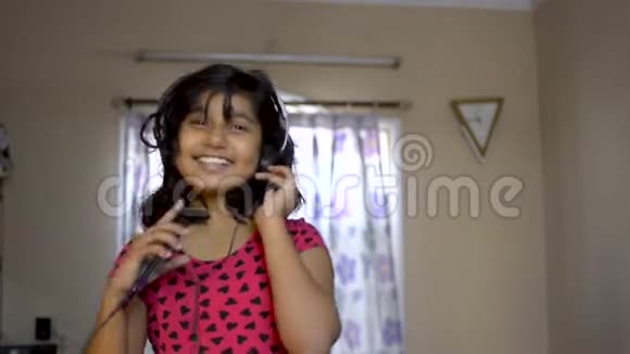 戴着耳机的印度亚裔白种人快乐女孩在手机上点头跳舞和唱歌视频的预览图
