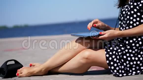 特写镜头女孩在平板电脑上工作的手腿上有鲜红的指甲指甲在海滩上在炎热的夏天视频的预览图