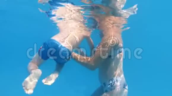 小妈妈在阳光明媚的日子里支持小儿子在游泳池游泳的慢动作水下视频视频的预览图