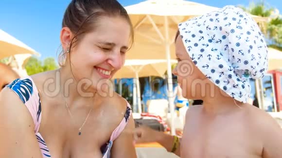 4k视频快乐微笑男孩涂防晒霜紫外线乳霜在沙滩妈妈脸上视频的预览图
