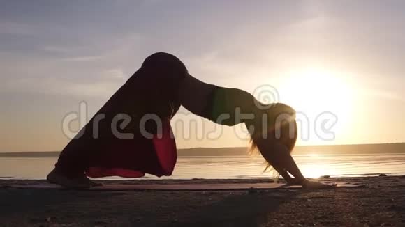 日落海滩上的美丽镜头女人在垫子上做瑜伽后弯乌尔德瓦穆卡什万萨纳慢动作视频的预览图